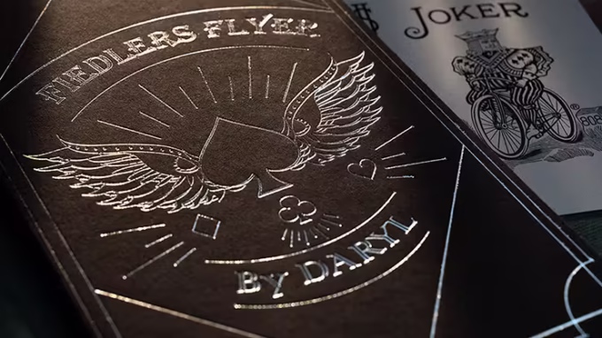 Detalle del diseño Fiedler's Flyer de Daryl con grabado en negro y plata junto a carta Joker.