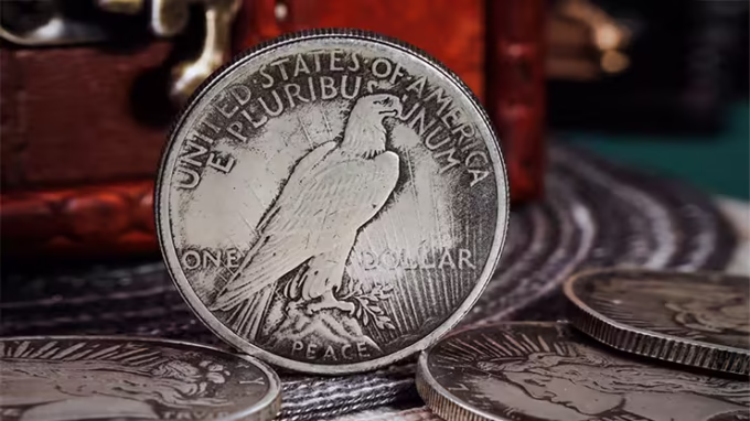 Reverso de la réplica Dólar de la Paz de 1921 mostrando un águila con detalles realistas, junto a otras monedas y un cofre vintage.