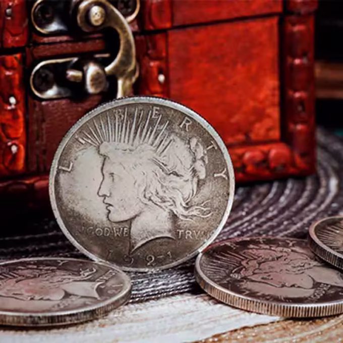 CS Réplicas Dólar de la Paz de 1921 con detalles realistas, acompañada de otras monedas y un cofre vintage