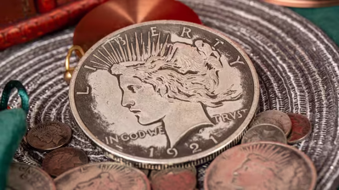 Moneda Jumbo Dollar de la Paz de N2G rodeada de monedas más pequeñas, destacando su diseño de perfil de Liberty, colocado sobre un tapete texturizado.