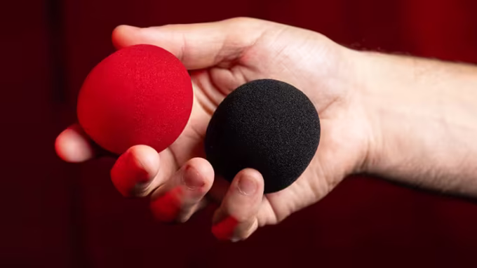 Bolas de Esponjas que Cambian de Color (rojo y negro) de Murphy's Magic sostenidas en la mano.