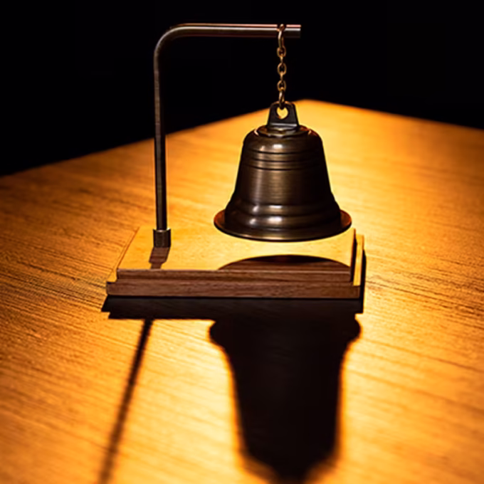 Spirit Bell by Tony Anverdi con campana metálica colgante, brazo en L y base de madera, iluminación cálida
